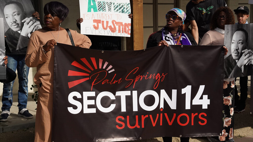 Two women hold a banner that reads Section 14 Survivors